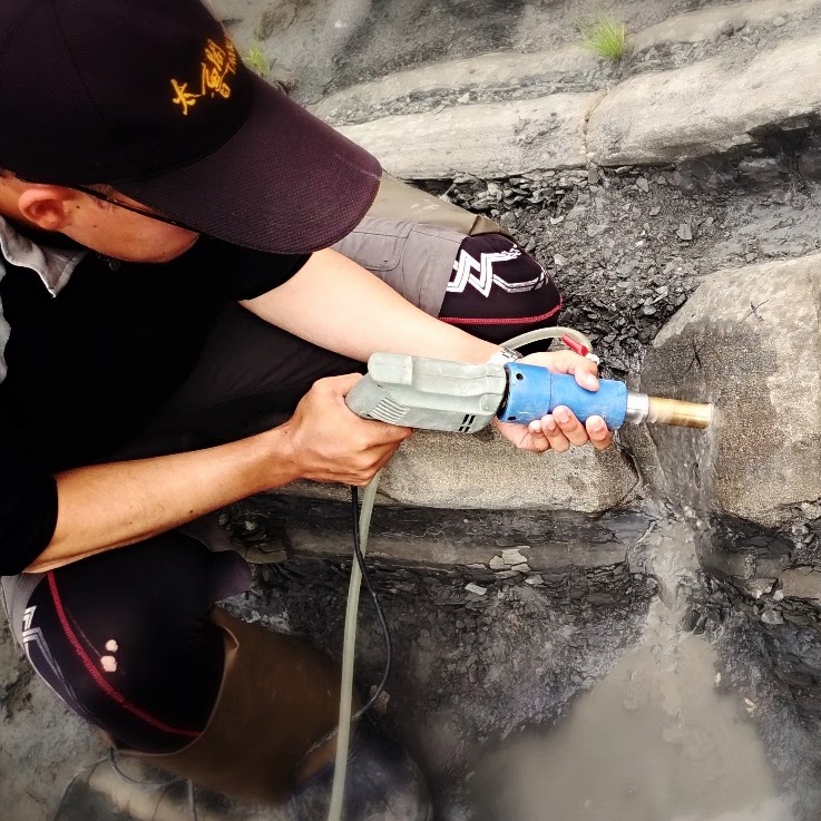 A person drilling an oriented sample from layered rock at an outcrop.