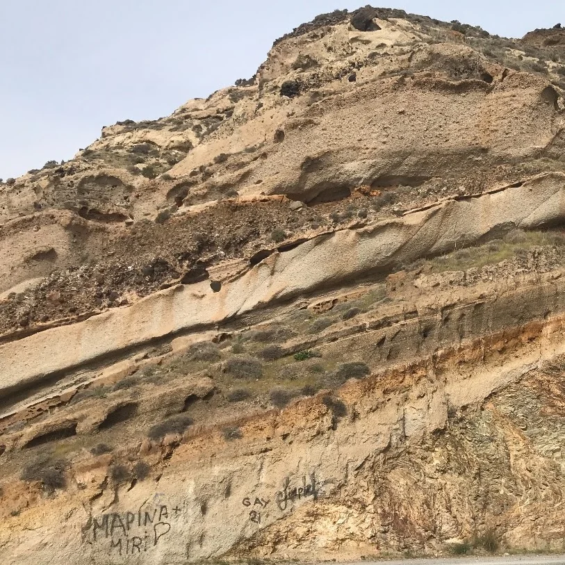 A road cut through tilted, layered sedimentary rock on a dry hillside.