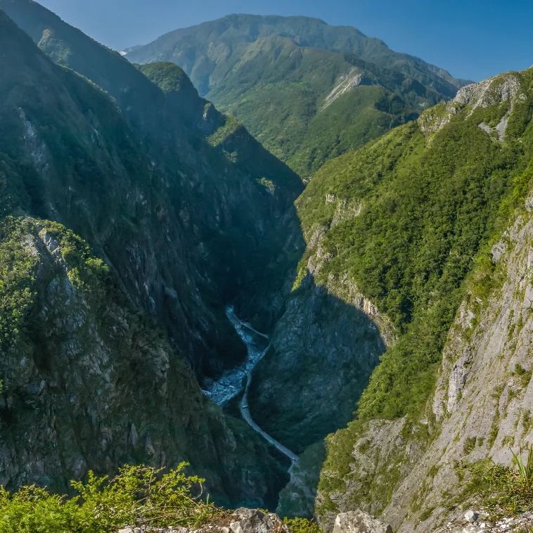 A deep mountain gorge with a braided river between steep, forested walls.